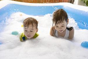 hermana y hermano divirtiéndose jugando con burbujas en la piscina en casa. juegos acuáticos de verano, felicidad familiar, felicidad infantil. foto