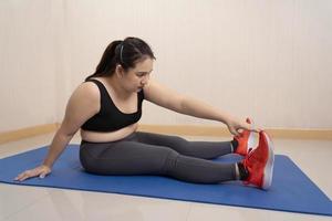 Beautiful fat woman in sportswear sits stretching on the floor before exercising at home. Dedicated to fitness. Sports motivation, sports concept, training endurance, Healthy weight loss, overweight photo