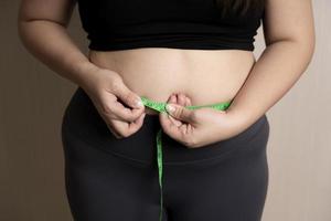 mano de mujer gorda sosteniendo grasa abdominal excesiva con cinta métrica. mujer gorda, panza gorda, gordita. concepto de control de peso saludable foto