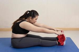 hermosa mujer gorda en ropa deportiva se sienta estirando en el suelo antes de hacer ejercicio en casa. dedicado al fitness. motivación deportiva, concepto deportivo, entrenamiento de resistencia, pérdida de peso saludable, sobrepeso foto