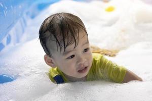 un niño asiático disfruta nadando y jugando con burbujas en una piscina inflable. juegos acuáticos de verano, felicidad familiar, felicidad infantil. foto