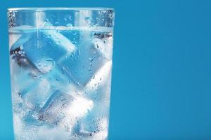 cubitos de hielo en un vaso con agua cristalina sobre un fondo azul.