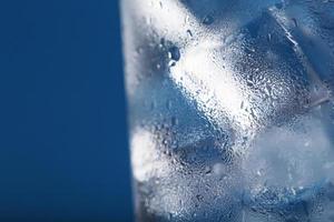 cubitos de hielo en un vaso con agua cristalina sobre un fondo azul.