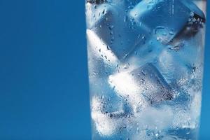 A glass with ice water and ice cubes on a blue background. photo