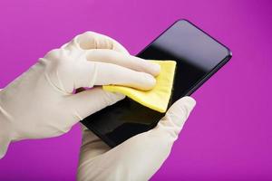 Cleaning a smartphone with a yellow napkin from dirt and viruses in rubber gloves on a pink background. photo