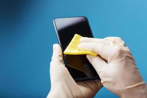 Disinfection of the smartphone with a yellow napkin with antibacterial impregnation in hand gloves. photo