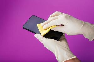 Preventive cleaning of a smartphone with a yellow napkin from dirt in rubber gloves on a pink background. photo