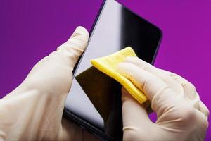 Preventive cleaning of a smartphone with a yellow napkin from dirt in rubber gloves on a pink background. photo