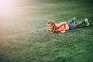 Fit woman in bright sports clothes to do burpees on the green grass photo