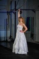 muscular bride in wedding dress doing exercises with a big weight in the gym. good physical shape healthy, lifestyle. photo