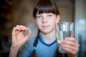 Capsules, pills in one hand, a glass of water in the other. The girl is holding the medicine in front of her. Close-up. photo