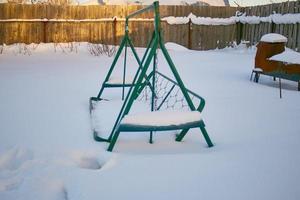 Snow-covered garden swing. wooden garden swing on chains, all in the snow. swing in winter. photo