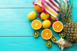 Citrus fresh food. Summer holidays. Orange, kiwi, pineapple, lemon and sea shell on blue wooden background. Vacation and summertime.Top view and copy space. Mock up photo