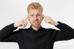 dolor de cabeza de hombre joven. chico pelirrojo con barba roja en proceso de pensamiento aislado. primer plano del rostro masculino. trabajo mental y mental. poder mental y creación de concepto de idea. hombre con camisa negra. dolor de cabeza foto