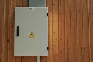 Knife switch and high voltage hazard sign on the wooden wall of house. Yellow electrical warning danger triangle symbol and metal security fence box. Closed lock electric panel transformer substation photo