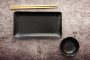 placa de pizarra negra con fondo de hormigón gris de palillos. endecha plana concepto de comida asiática foto