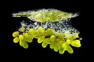 uvas verdes en agua salpicada sobre un fondo negro foto