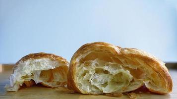 Close up a torn croissant, cross section of golden fresh baked French Croissant bakery, on wooden tray, blurred background, warm tone photo