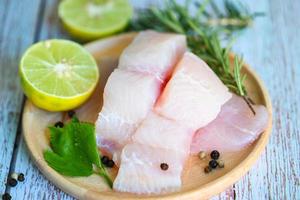 filete de pescado en un plato de madera con ingredientes apio para cocinar, filete de pescado pangasius crudo fresco con lima limón, carne dolly pescado tilapia bagre rayado foto