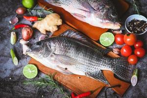 Tilapia with spice rosemary tomato lemon lime ginger garlic pepper chili on dark background, Fresh raw tilapia fish from the tilapia farm - top view photo