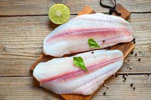 Meat dolly fish tilapia striped catfish, fish fillet on wooden board with ingredients for cooking, fresh raw pangasius fish fillet with herb and spices black pepper lemon lime photo