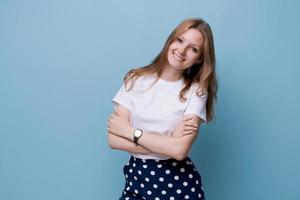 mujer joven sonriente de pie con los brazos cruzados en camiseta blanca y polka foto