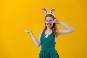 Shot happy girl in fluffy pink bunny ears, points fingers to side, demonstrates photo