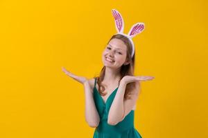 Dreamy happy young woman wearing pink with white bunny ears, holding face photo