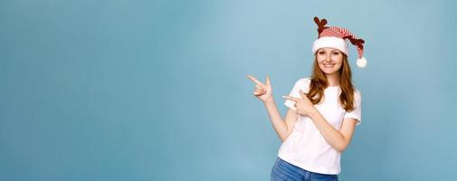 Cheerful santa girl in funny decorative deer antlers, pointing with forefinger photo