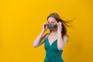 Beautiful young woman protection mask wearing for coronavirus disease on yellow photo