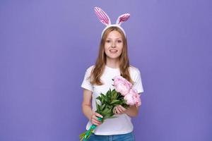 Cute young woman with pink easter bunny ears on purple background in white photo