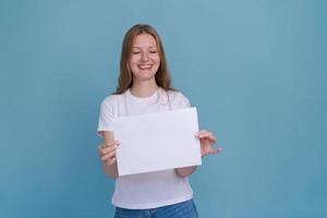 Retrato alegre joven mujer caucásica sonriendo sosteniendo pancarta en blanco blanco foto