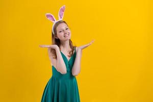 Shot happy girl in fluffy pink bunny ears, points fingers to side, demonstrates photo