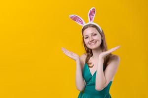 Dreamy happy young woman wearing pink with white bunny ears, holding face photo
