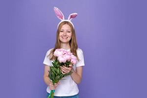 Cute young woman with pink easter bunny ears on purple background in white photo