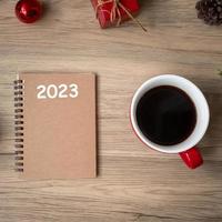 Cuaderno 2023, taza de café negro y regalo de navidad en mesa de madera, vista superior y espacio para copiar. navidad, feliz año nuevo, objetivos, resolución, lista de tareas, estrategia y concepto de plan foto