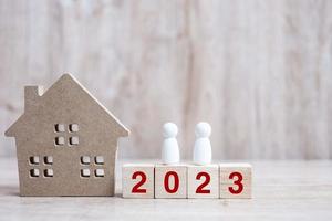 2023 feliz año nuevo con modelo de casa y gente sobre fondo de madera. conceptos bancarios, inmobiliarios, de inversión, financieros, de ahorro y de resolución de año nuevo foto