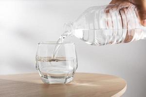 Man's hand holding drinking water bottle and pouring water into glass on wooden table photo