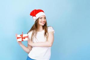 Young caucasian woman in christmas hat and with gifts in white t-shirt smiles photo