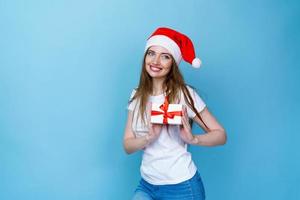 Young caucasian woman in christmas hat and with gifts in white t-shirt smiles photo