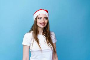 chica alegre con sombrero de santa posando y sonriendo con una sonrisa con dientes en azul foto