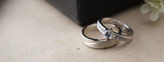 anillo de bodas de oro blanco con un láser de pájaro en la superficie del anillo. con fondo de caja de anillos negra y flores artificiales. a la izquierda hay un espacio vacío para completar el texto foto