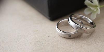 White gold wedding ring with a bird laser on the ring surface. With a black ring box background and artificial flowers. On the left there is an empty space to fill in text photo