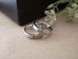 anillo de bodas sobre una base de madera con un fondo de anillo negro y flores artificiales foto