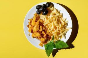 Nuggets with sauce in a plate with French fries and olives on a yellow background with red napkins. hard shadows. photo