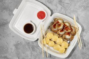 Delicious sushi rolls in disposable plastic boxes. The hand takes a roll with chopsticks. Food delivery service concept, flat stacking photo