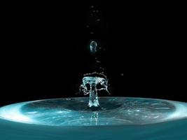 A splash of blue water with a drop flying from above on a black background photo