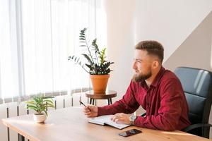 Budget planning. Pensive bearded man writing in a notebook while sitting photo