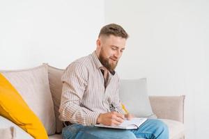 An image concentrated young bearded man sitting in notes on couch at home photo