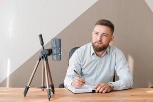 Cheerful bearded young man leading an online meeting using smartphone writing photo